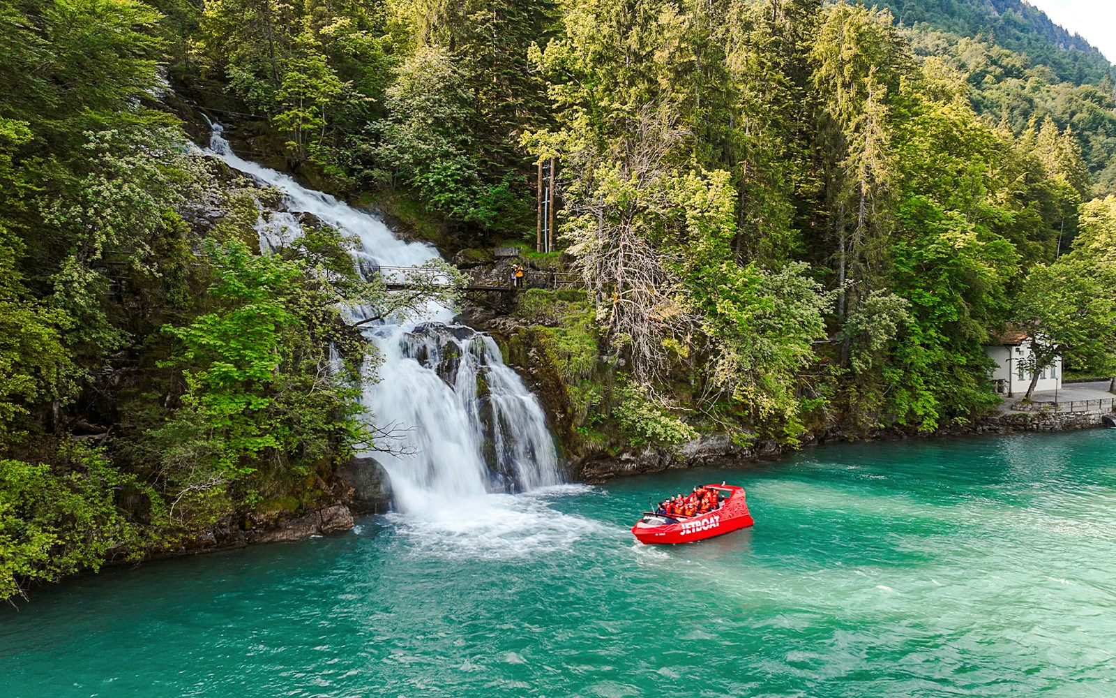 Jetboat on Lake Brienz near a waterfall surrounded by lush forest.