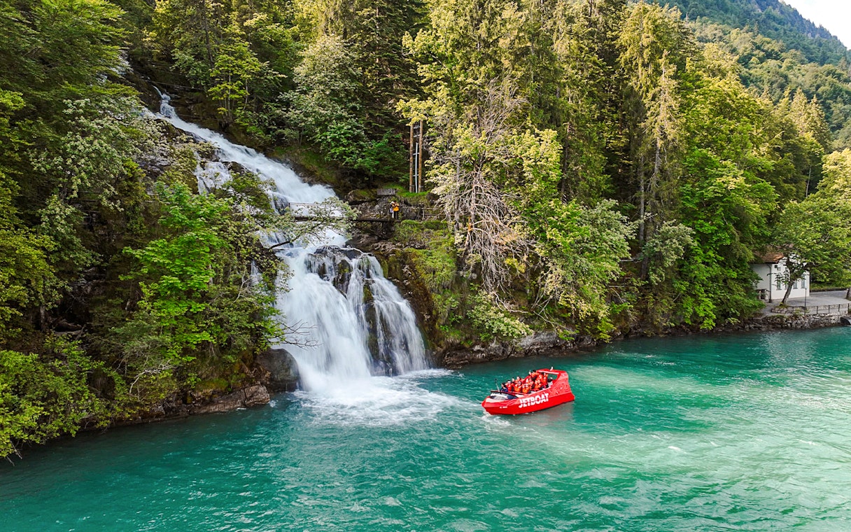 Jetboat on Lake Brienz near a waterfall surrounded by lush forest.