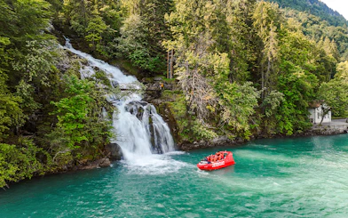 Jetboat on Lake Brienz near a waterfall surrounded by lush forest.