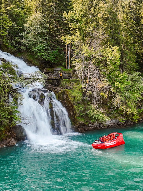 Jetboat on Lake Brienz near a waterfall surrounded by lush forest.
