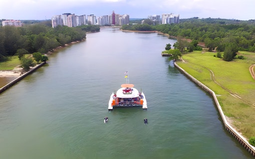 Catamaran sailing through a river with cityscape in the background at Dickson Dragon Cruise Port Dickson.