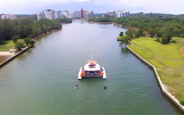 Catamaran sailing through a river with cityscape in the background at Dickson Dragon Cruise Port Dickson.