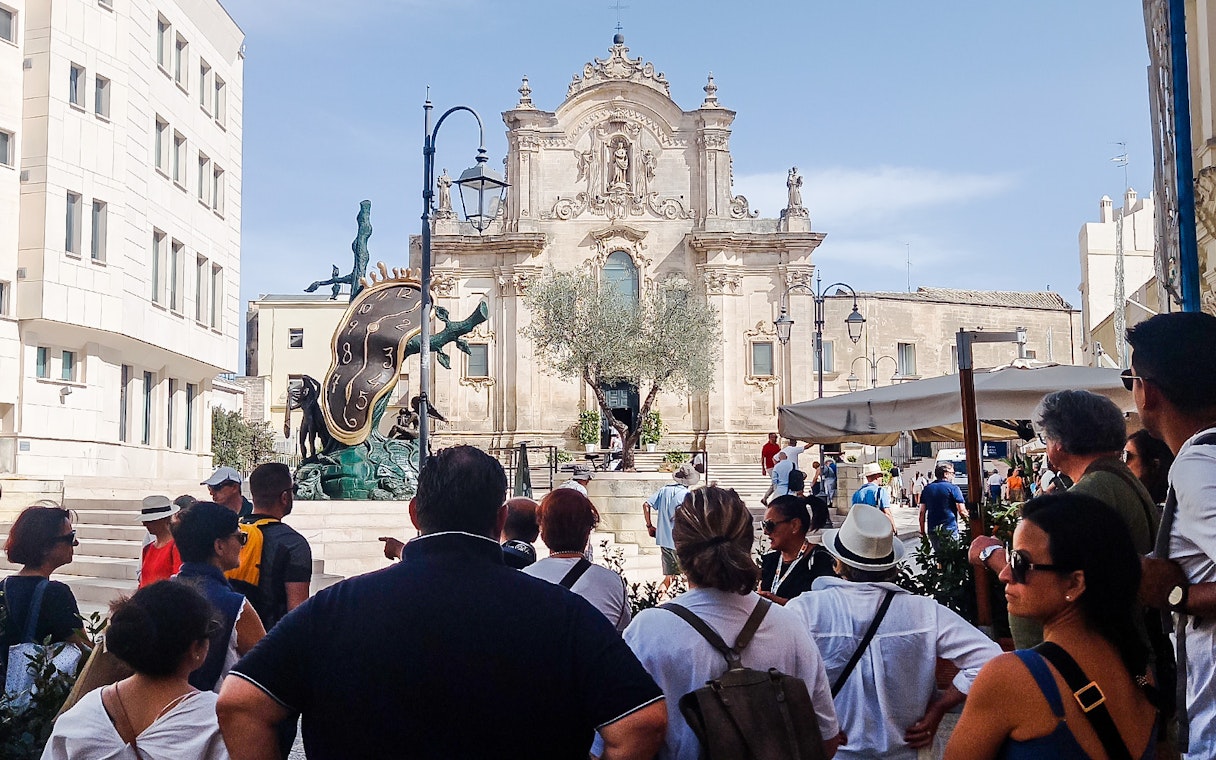 Tour group viewing Salvador Dalí sculpture and historic building on bus tour with audio guide.