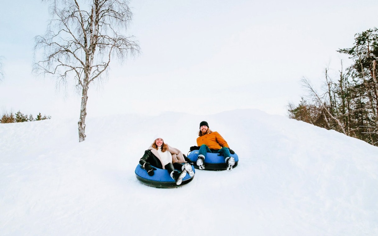Guests sledding on snow tubes outside Arctic SnowHotel.