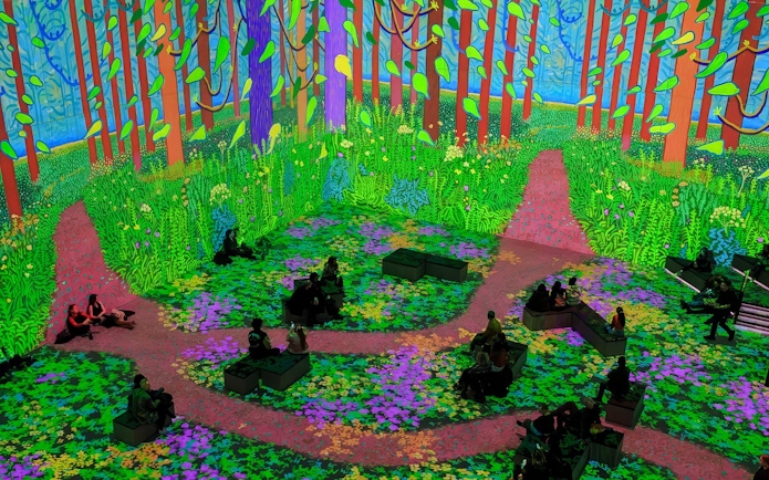 Immersive digital forest scene from David Hockney: Bigger & Closer exhibition with seated visitors.