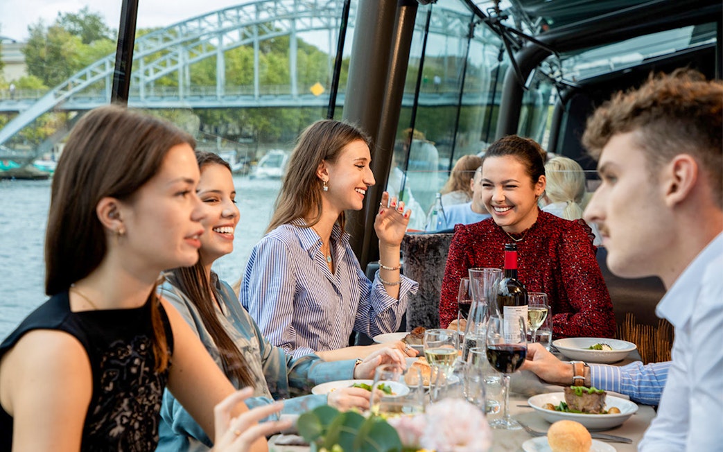 People dining on a Seine River lunch cruise with a view of a bridge in Paris.