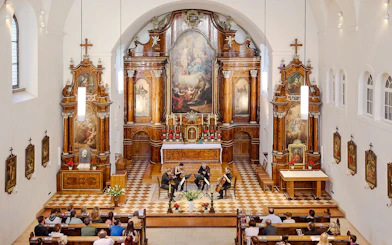 String quartet performing in Minoritenkirche, Vienna, with ornate altar backdrop.