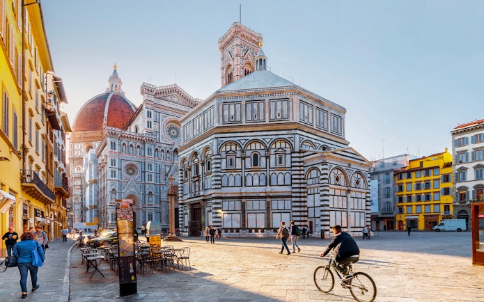 Baptistery and Florence Cathedral in Piazza del Duomo, Florence, with people walking and cycling.