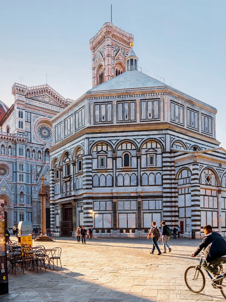Baptistery and Florence Cathedral in Piazza del Duomo, Florence, with people walking and cycling.