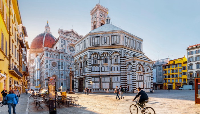 Baptistery and Florence Cathedral in Piazza del Duomo, Florence, with people walking and cycling.