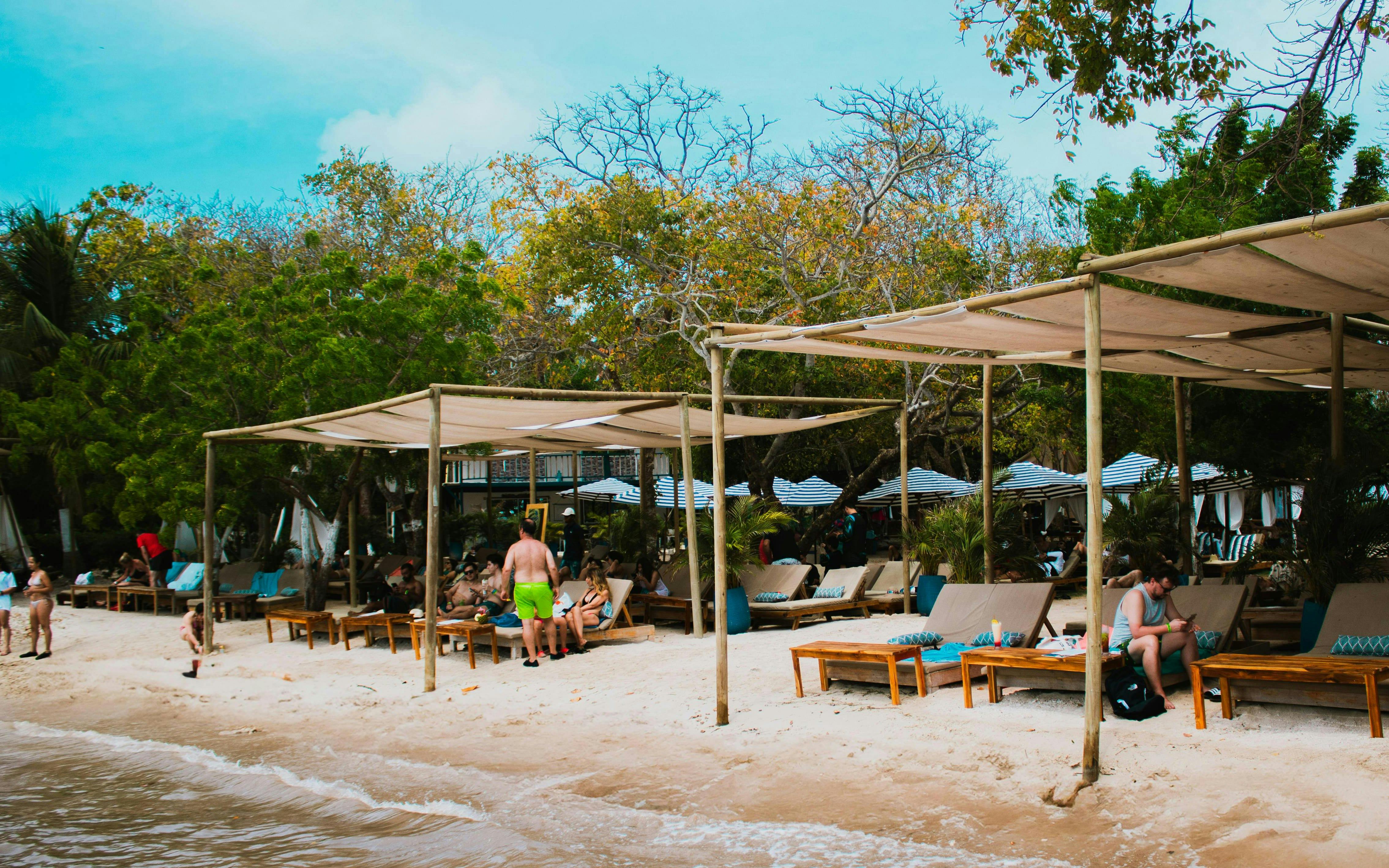 Shaded seating area at Islabela beach club, Rosario Islands, with white sand and lounge chairs.