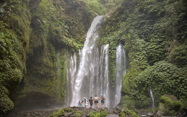 Tourists enjoying Tiu Kelep Waterfalls in lush Lombok, Indonesia.