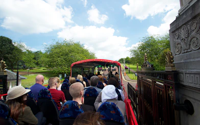 Open-top bus with tourists on Belfast Hop-On Hop-Off Tour passing through a park.