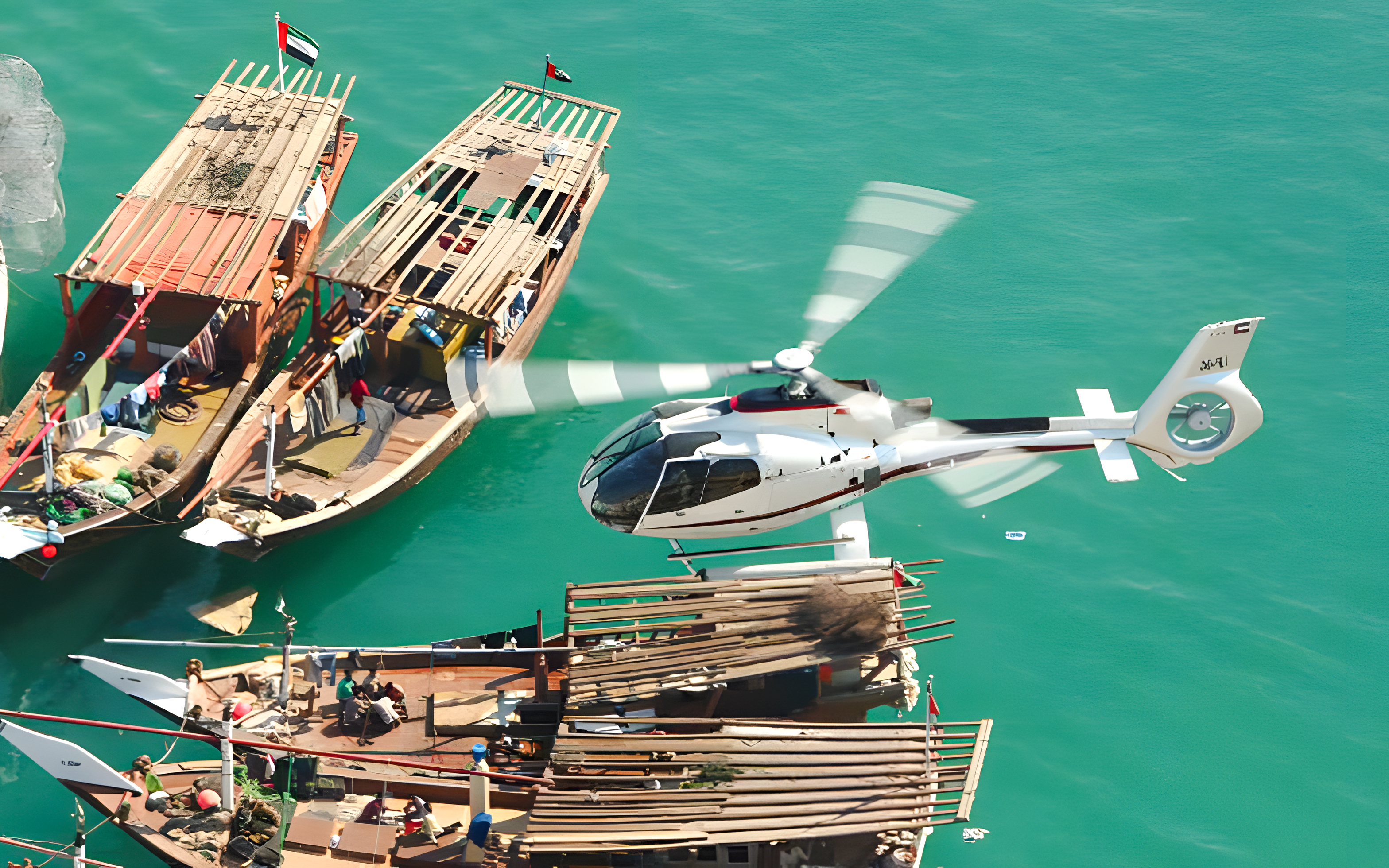 Helicopter flying over traditional boats on Dubai's turquoise waters.