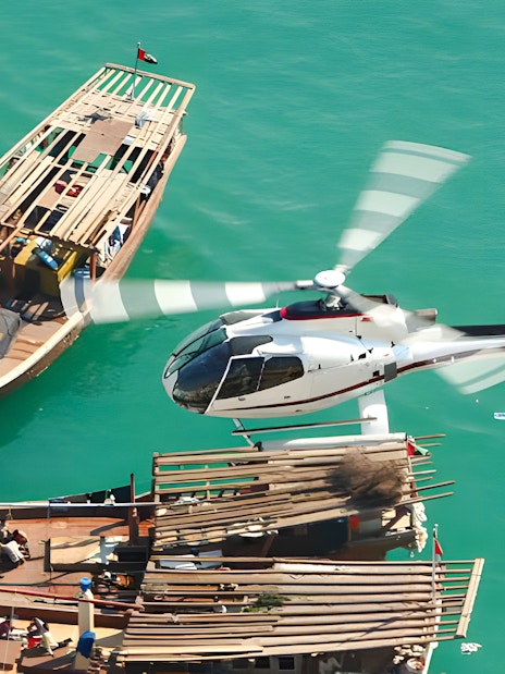 Helicopter flying over traditional boats on Dubai's turquoise waters.