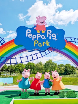 Staff in Peppa Pig costumes at Peppa Pig Park, Günzburg, under a colorful arch.