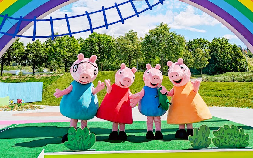 Staff in Peppa Pig costumes at Peppa Pig Park, Günzburg, under a colorful arch.