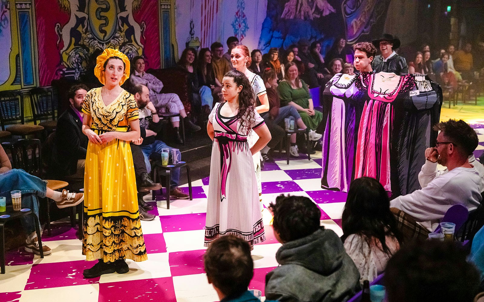 Actors performing "Plied and Prejudice" on a colorful stage with an audience in London theater.
