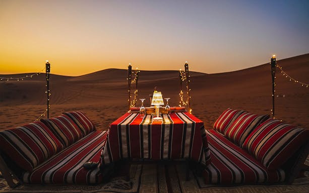 Private dinner setup in desert safari with sunset and string lights.