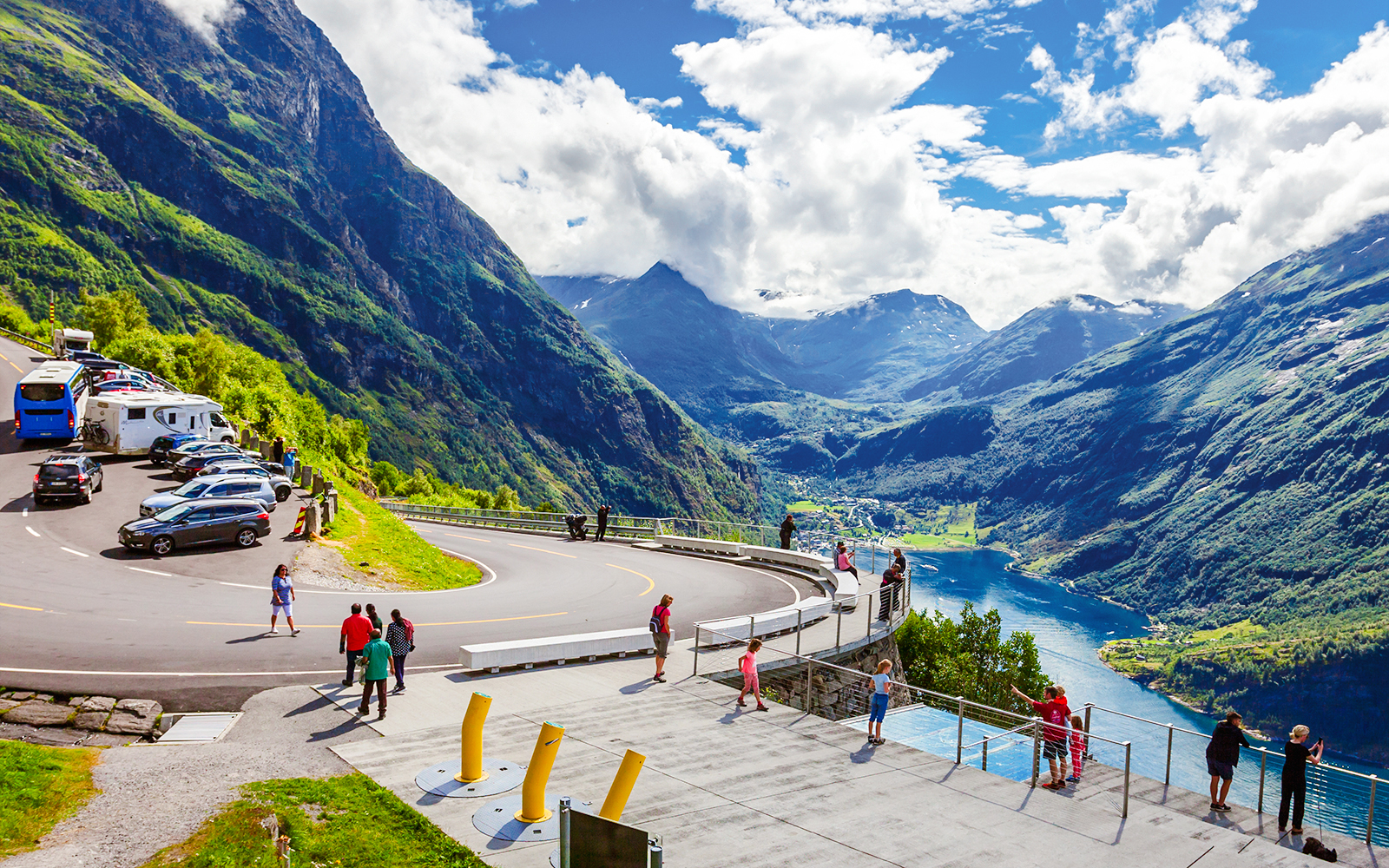 Viewing platform overlooking Geirangerfjord, Norway with tourists and parked vehicles.