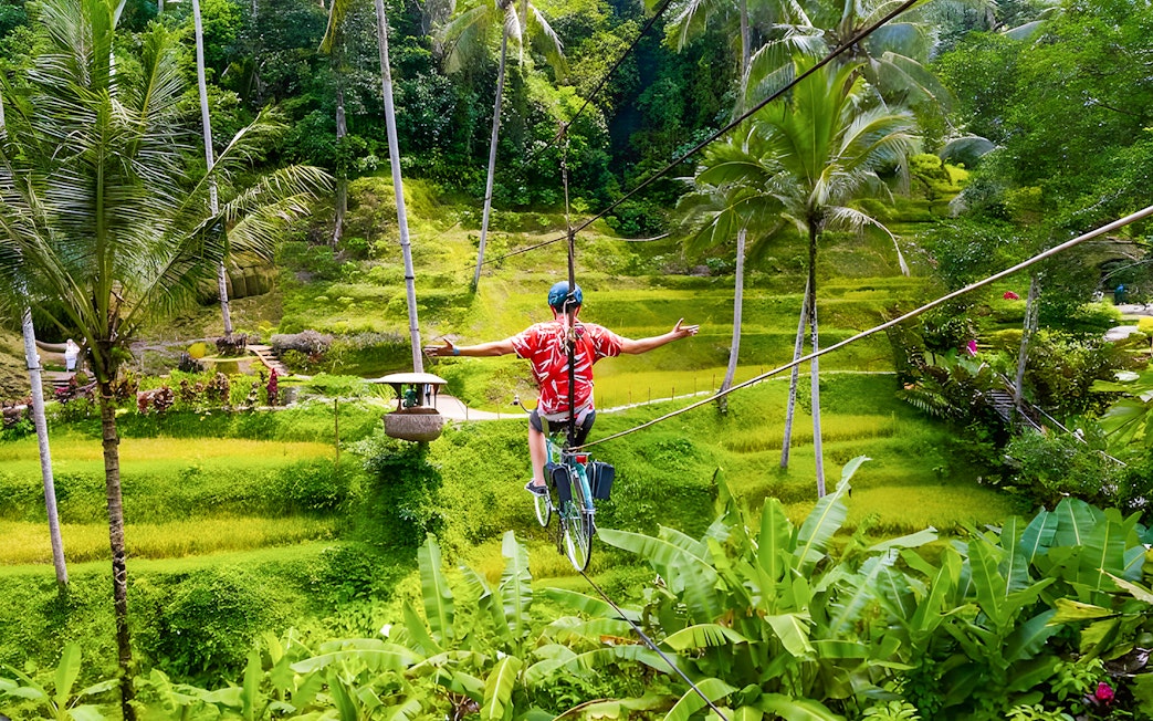 Man riding a sky bike over lush green rice terraces at Alas Harum, Bali.
