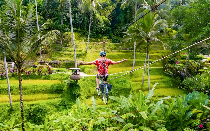 Man riding a sky bike over lush green rice terraces at Alas Harum, Bali.
