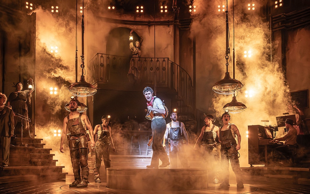 Stage performance of Hadestown with actors in industrial costumes and dramatic lighting.
