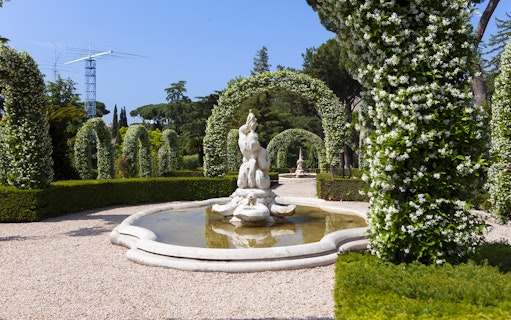 Vatican Gardens fountain surrounded by flowering arches on open bus tour.