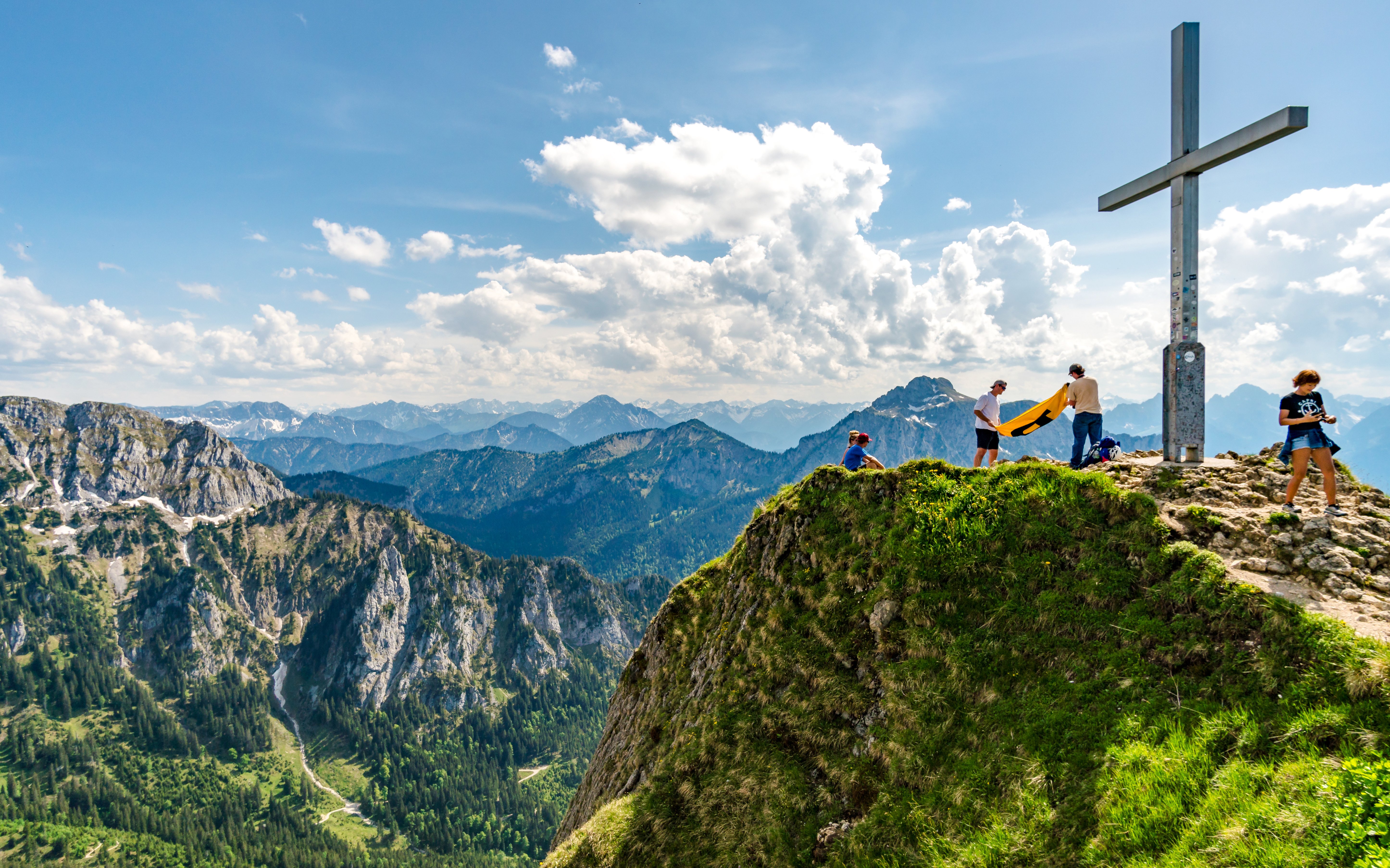 Hikers at Tegelberg Summit Platform with mountain views and a large cross.