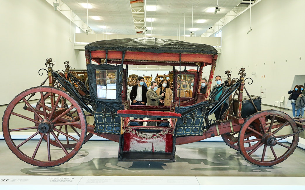 Antique coach display at the National Coach Museum, Lisbon, with visitors observing.