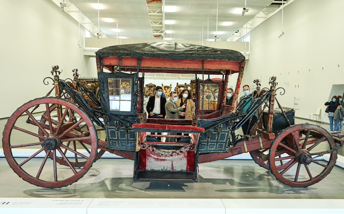 Antique coach display at the National Coach Museum, Lisbon, with visitors observing.