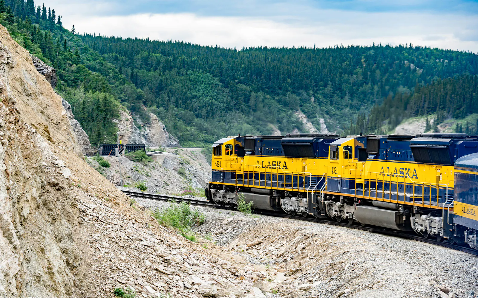 Alaska Railroad train traveling through forested mountain landscape.