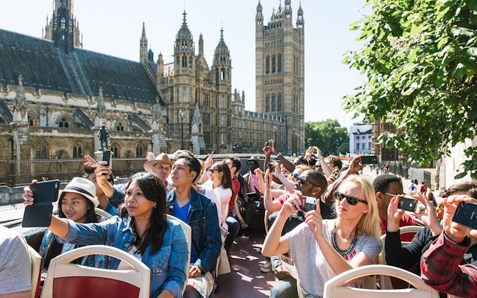 Tourists on a Big Bus near Big Ben, London, taking photos of the landmark.