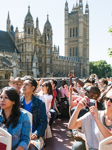 Tourists on a Big Bus near Big Ben, London, taking photos of the landmark.
