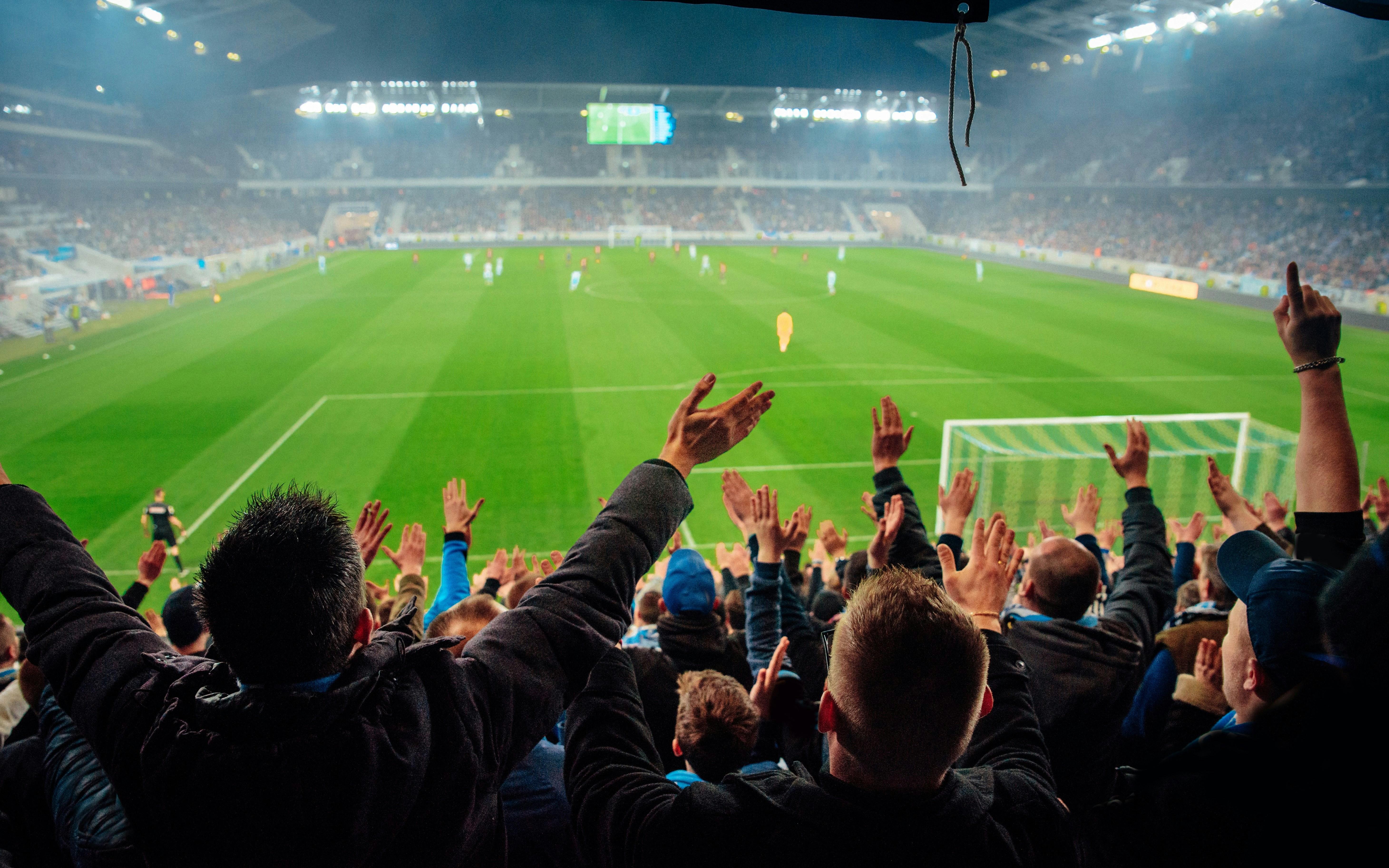 Football fans cheering in a crowded stadium during a soccer match.