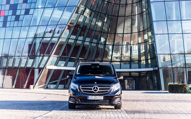 Private transfer vehicle in front of modern glass building at Krakow Airport.