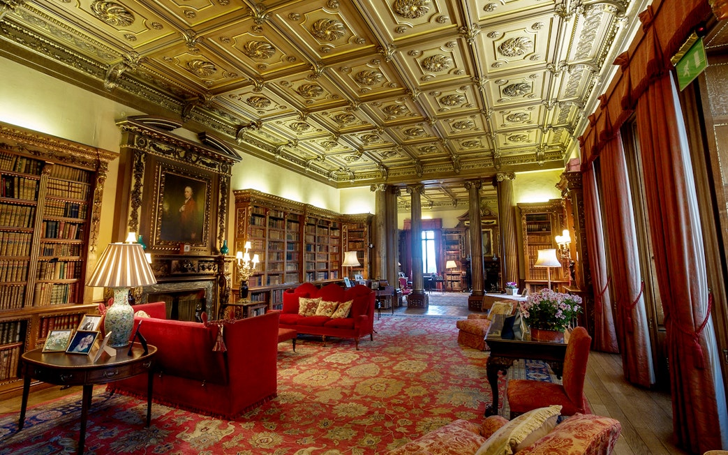 Highclere Castle library with ornate ceiling, bookshelves, and red sofas on Downton Abbey tour.