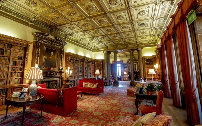 Highclere Castle library with ornate ceiling, bookshelves, and red sofas on Downton Abbey tour.