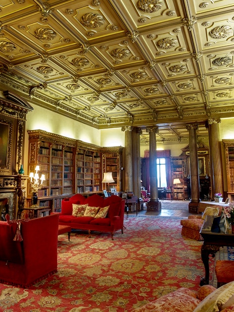 Highclere Castle library with ornate ceiling, bookshelves, and red sofas on Downton Abbey tour.