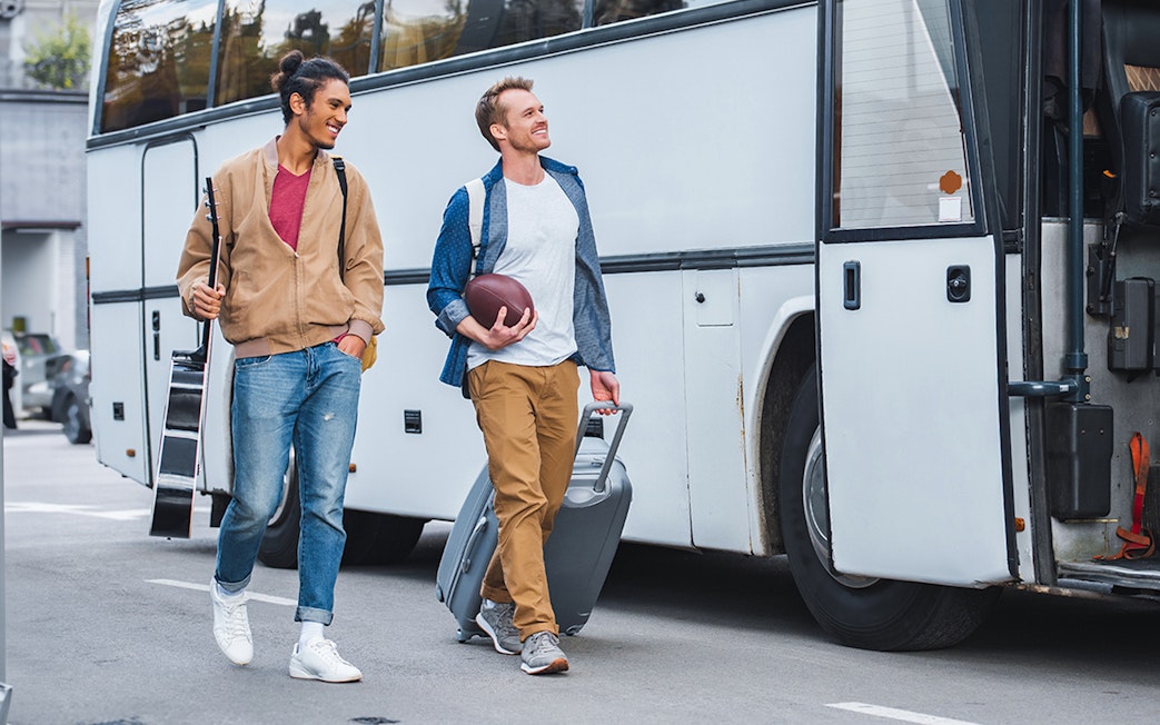 Two passengers boarding a bus with luggage and a guitar.