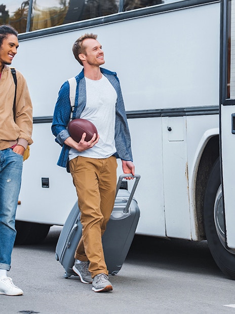 Two passengers boarding a bus with luggage and a guitar.