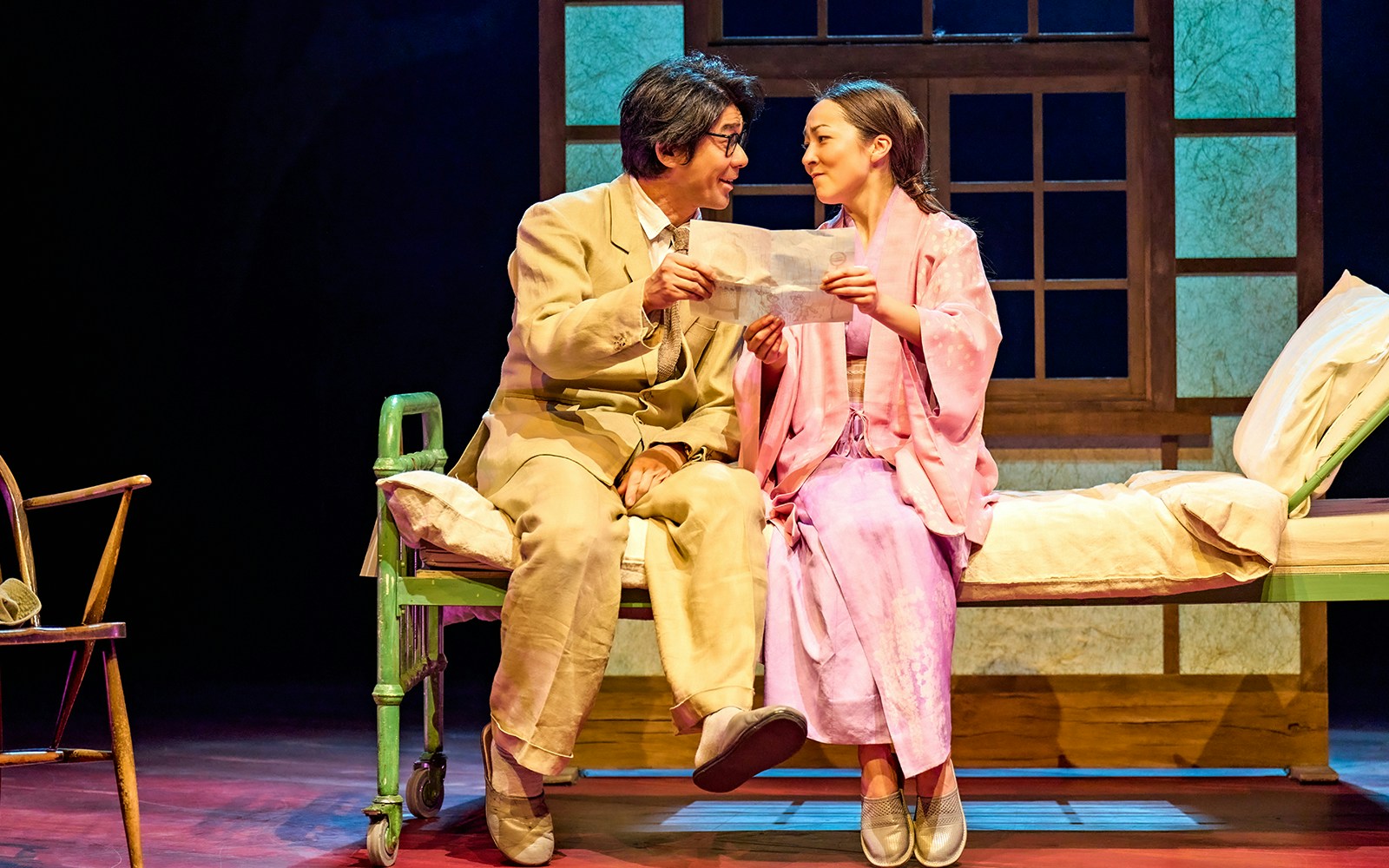 Two actors in a stage scene from "My Neighbour Totoro," sharing a moment on a bed.