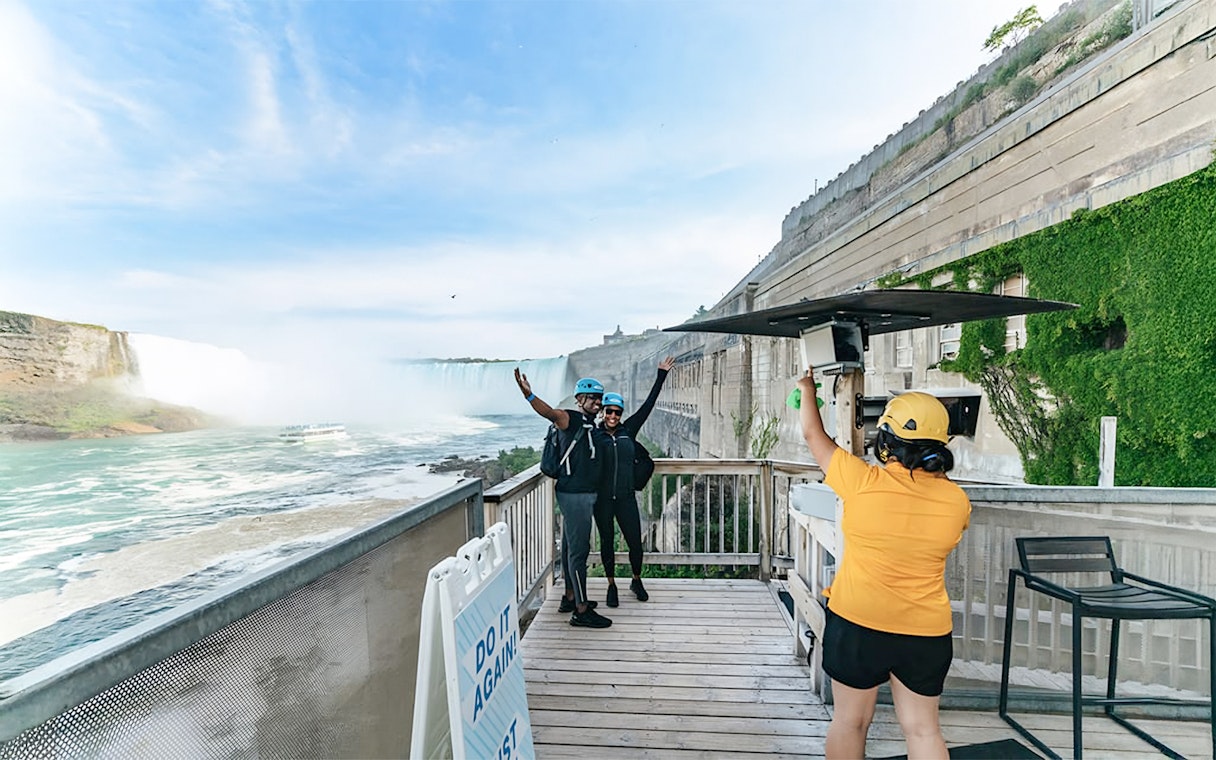 Visitors preparing for a zipline ride with a view of Niagara Falls in the background.