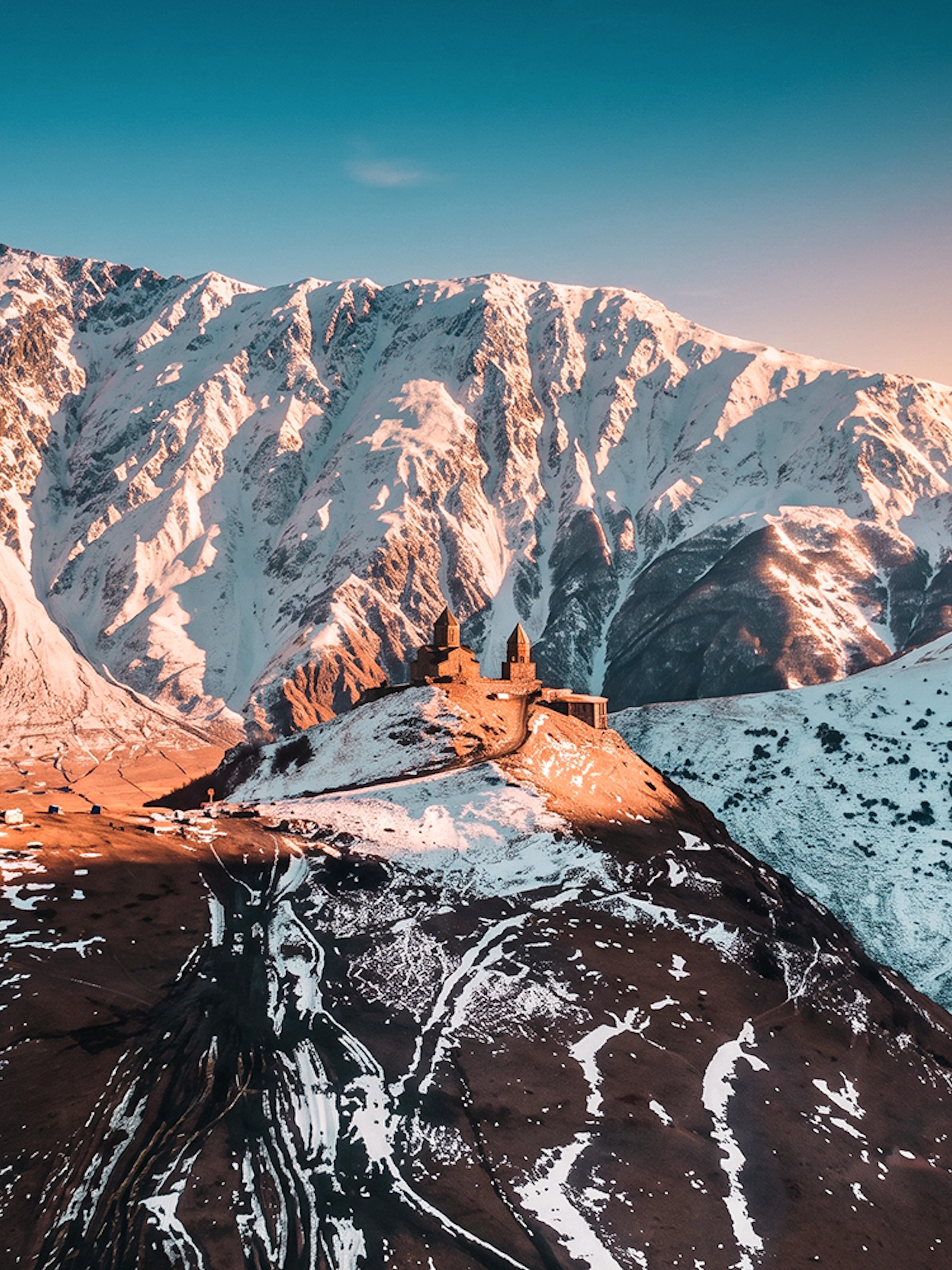 Gergeti Trinity Church on a snowy mountain in Georgia with a sunset backdrop.