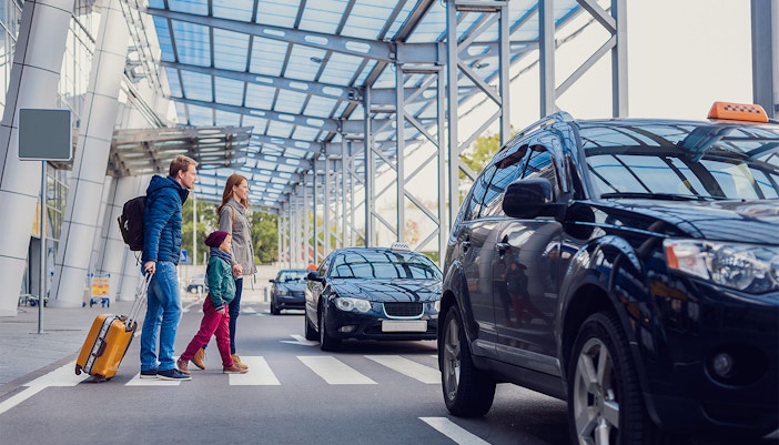 Family crossing road with parked taxis nearby.