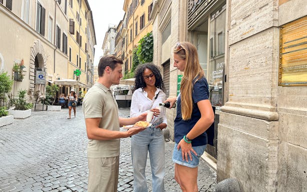 Tourists enjoying wine and pizza on a cobblestone street in Rome.