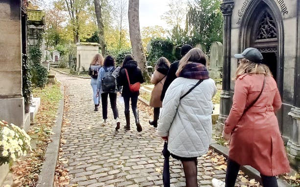 Visitors exploring Père Lachaise Cemetery, Paris, France, surrounded by historic tombstones and lush greenery.
