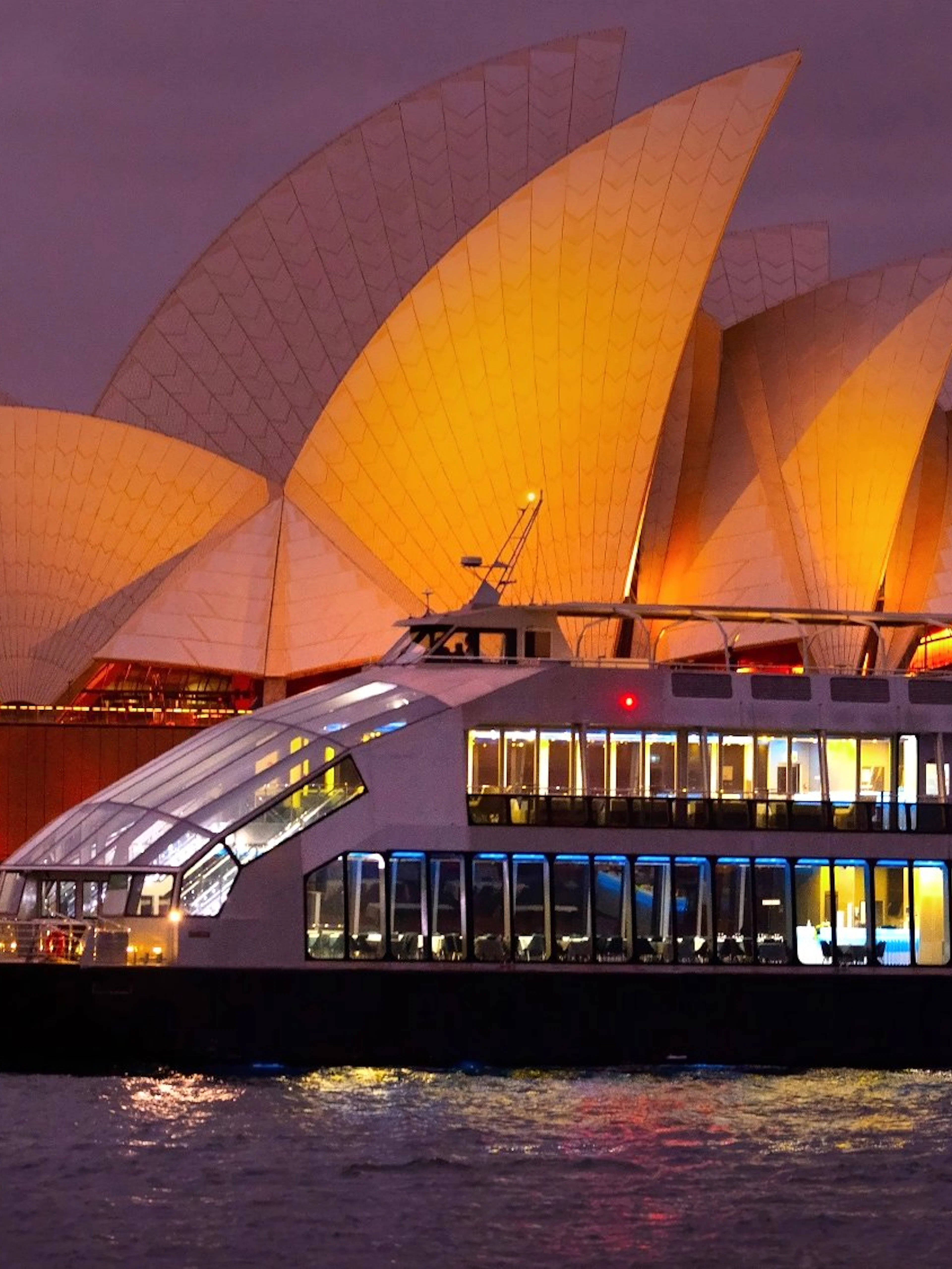 Glass boat dinner cruise with Sydney Opera House illuminated in the background.