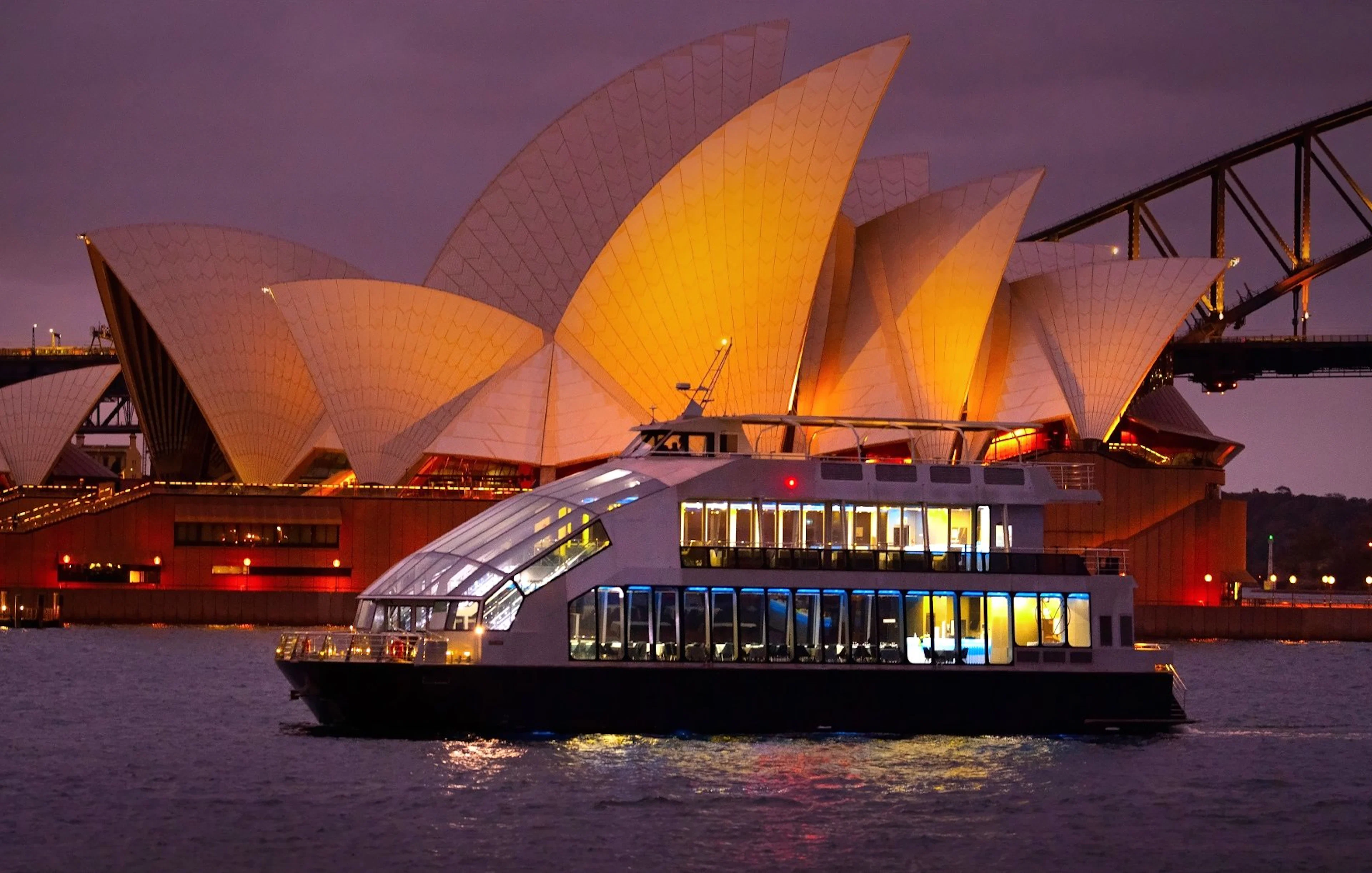Glass boat dinner cruise with Sydney Opera House illuminated in the background.
