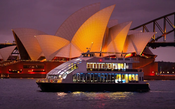 Glass boat dinner cruise with Sydney Opera House illuminated in the background.